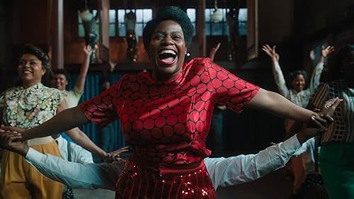 A still from the 2023 film The Color Purple. Celie, in a red dress, is front and center in a choreographed song and dance sequence.