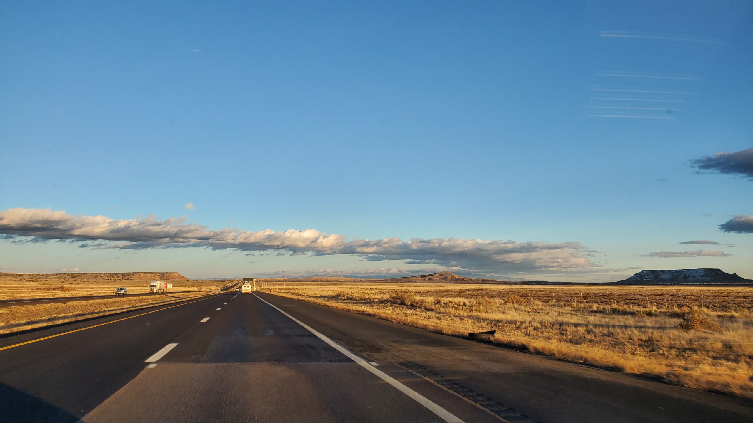 Photo of a desert highway. The horizon is low, ground flat save for a few mesas in the distance.