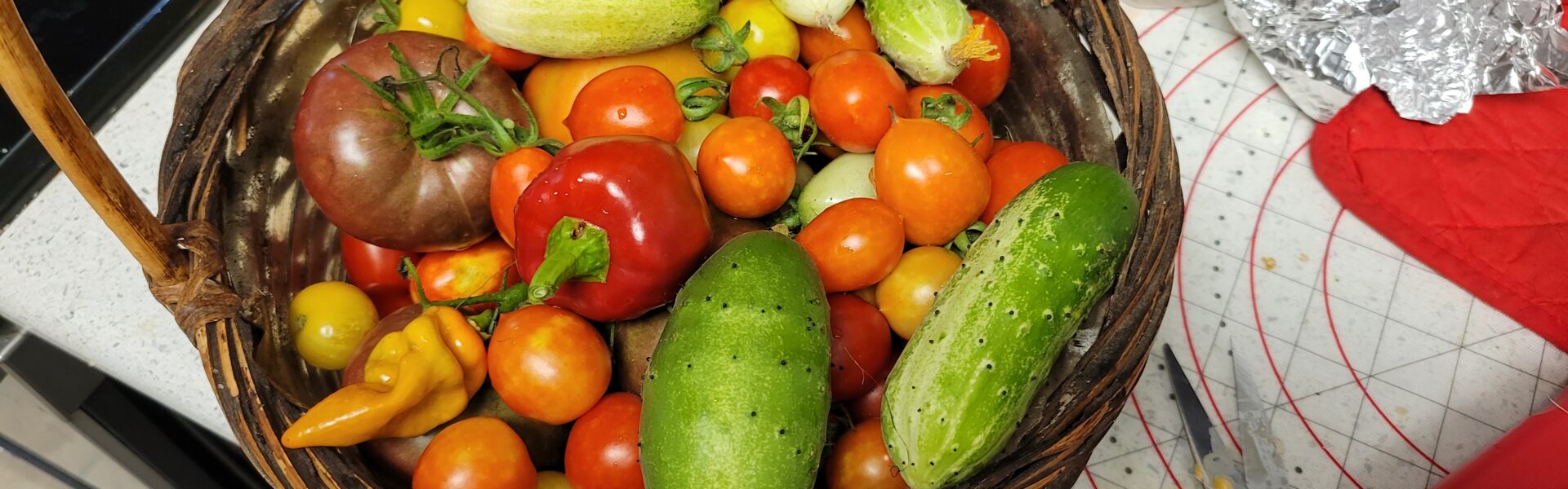 Photo of a basket full of garden-grown vegetables: cucumbers, peppers, tomatoes.