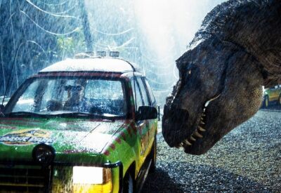 Screen cap from the film Jurassic Park. A Tyrannosaurus Rex leans close to peer inside the windows of a Jeep.