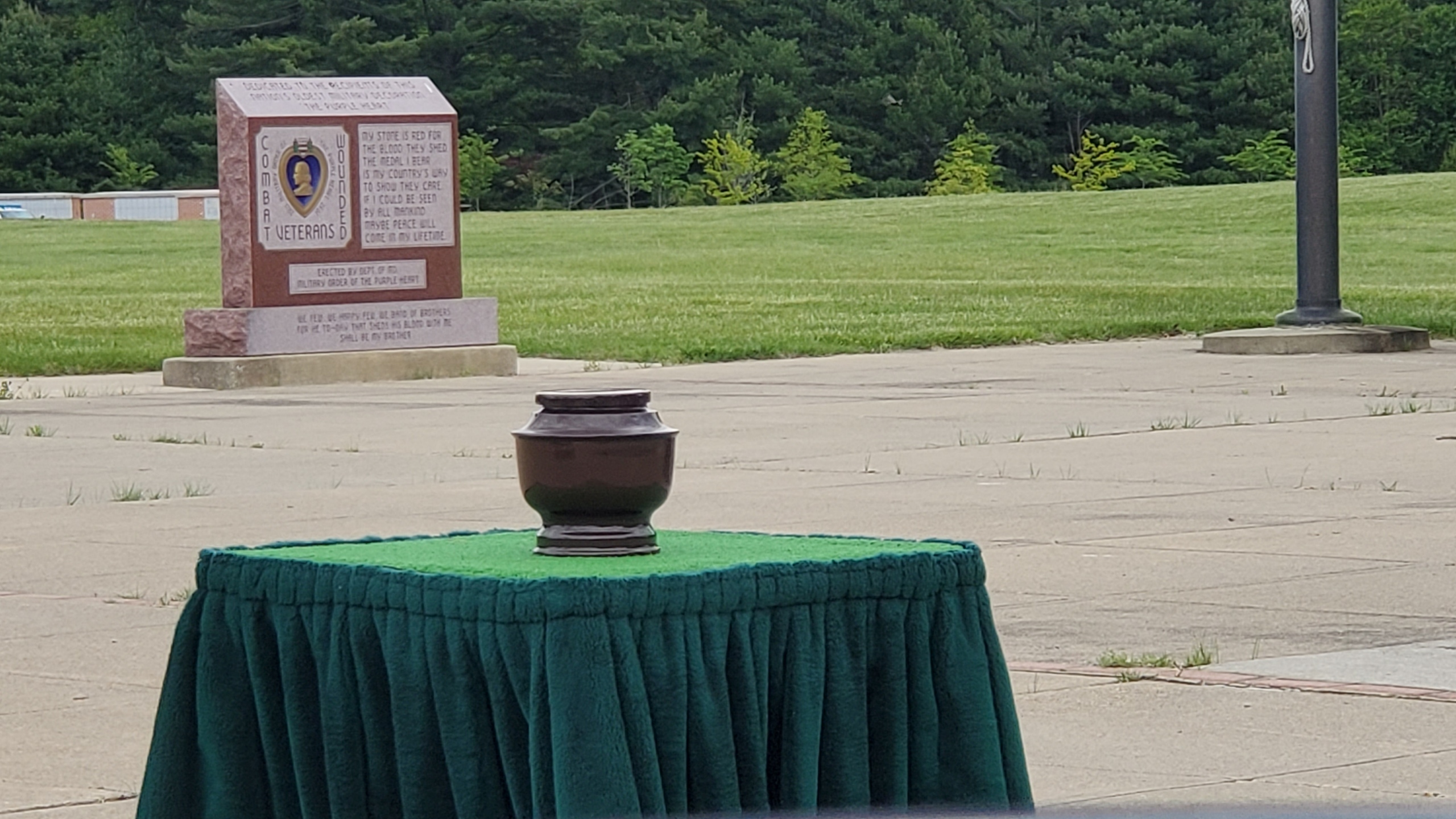 Photo of an urn sitting outdoors on a square platform dressed in green cloth. The location is a military cemetery.